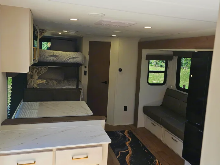 Modern rv rental interior: bunk beds, sleek kitchenette, and a cozy sofa by windows offering outdoor views, ready for your adventure.. Grand Design Transcend Xplor 2026