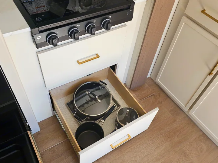 Efficient RV rental kitchen with a modern stovetop and an open drawer revealing neatly stored pots and pans.. Grand Design Transcend Xplor 2026