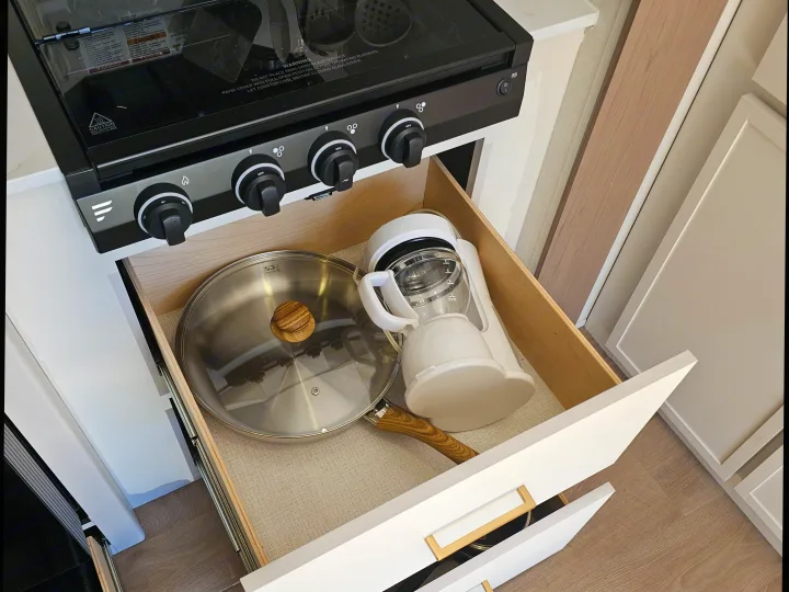 Compact RV rental kitchen showcasing a black stovetop and an open drawer with a pan and white coffee maker.. Grand Design Transcend Xplor 2026