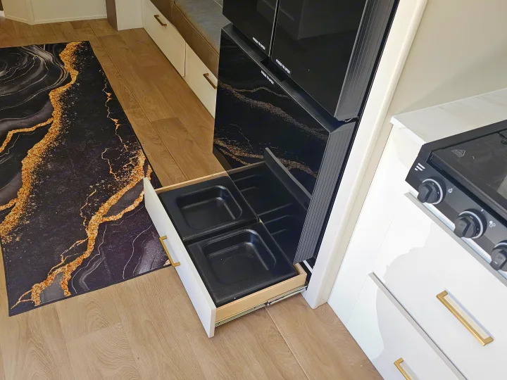Modern RV rental kitchenette: A sleek black appliance, pull-out drawer with organizers, light wood floor, and black rug.. Grand Design Transcend Xplor 2026