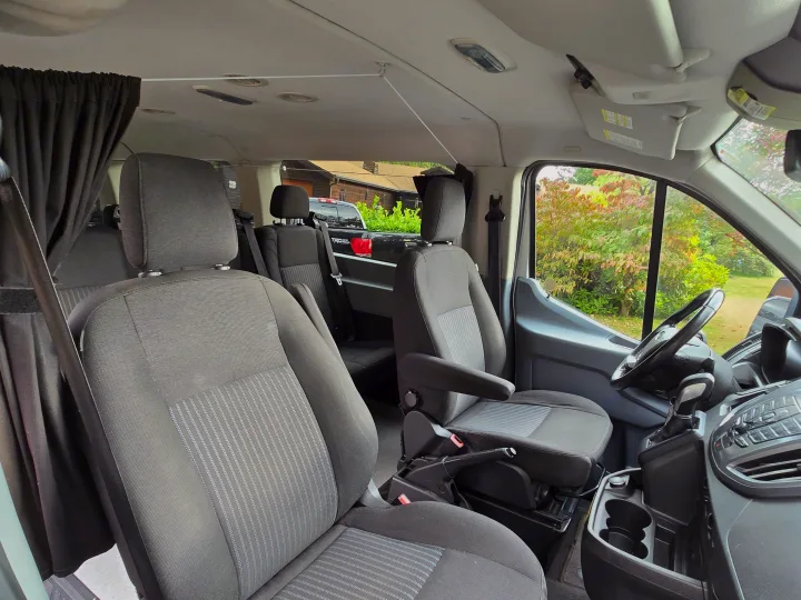rv rental interior: view from passenger side, showing multiple rows of cloth seats, privacy curtains, and driver's area.. Ford Transit 2017