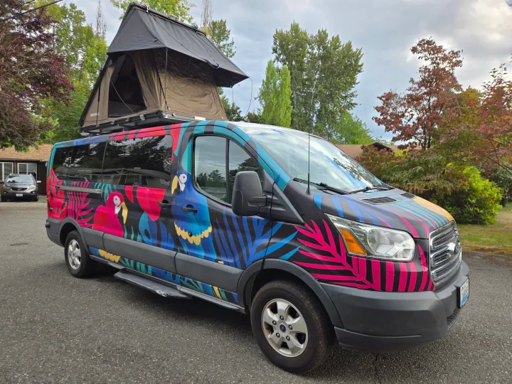 This vibrant RV rental van, featuring colorful parrot and leaf graphics, is equipped with a rooftop tent for adventures.. Ford Transit 2017