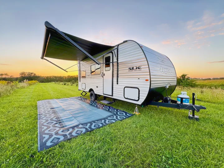 Serene RV rental camping: A travel trailer with an extended awning and mat is parked in a green field at sunset.. Jayco Jay Flight SLX Sport Edition 2026