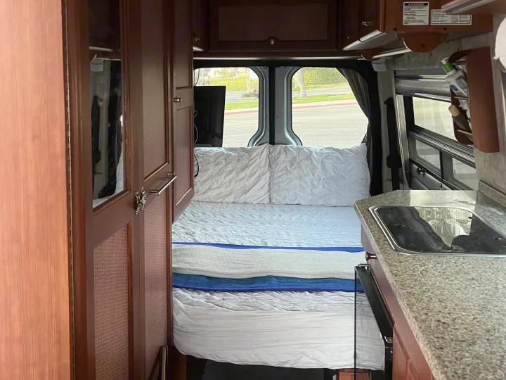 RV rental interior: a comfy bed with white linens, wood cabinetry, and a granite-top kitchen with a sink.. Roadtrek Roadtrek Class B 2007