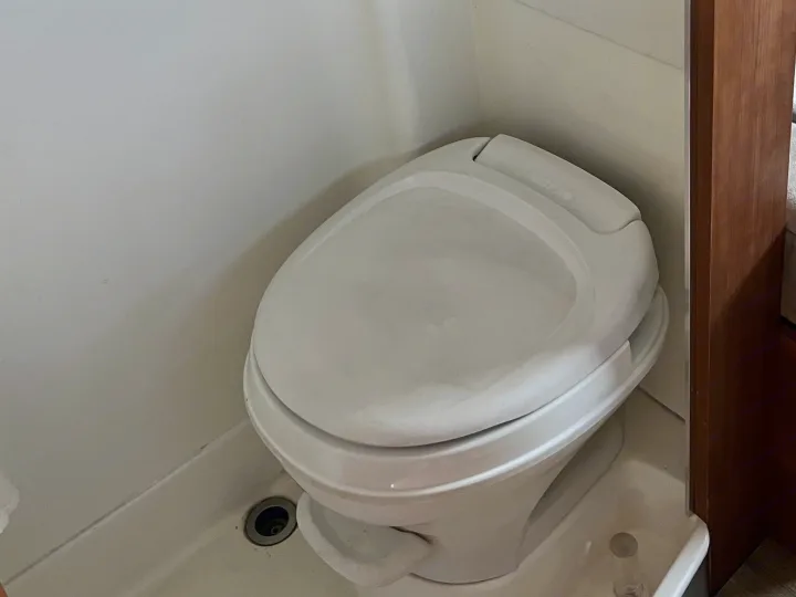 White compact toilet with closed lid inside an RV rental bathroom, showing a floor drain.. Roadtrek Roadtrek Class B 2007