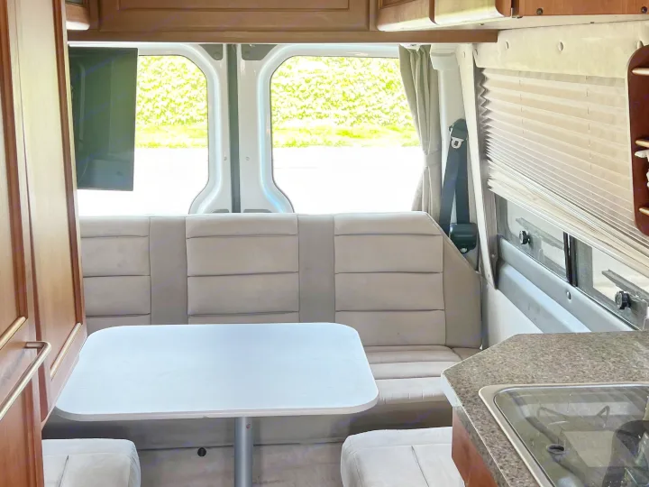 Experience comfort in this rv rental! Dinette area with table, bench seating, TV, and scenic window view, plus a partial kitchen.. Roadtrek Roadtrek Class B 2007