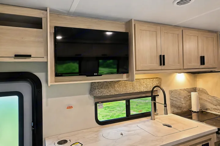 Bright RV rental kitchen with light wood cabinets, TV, modern sink, and cooktop, ready for your next adventure.. Forester Classic 2021