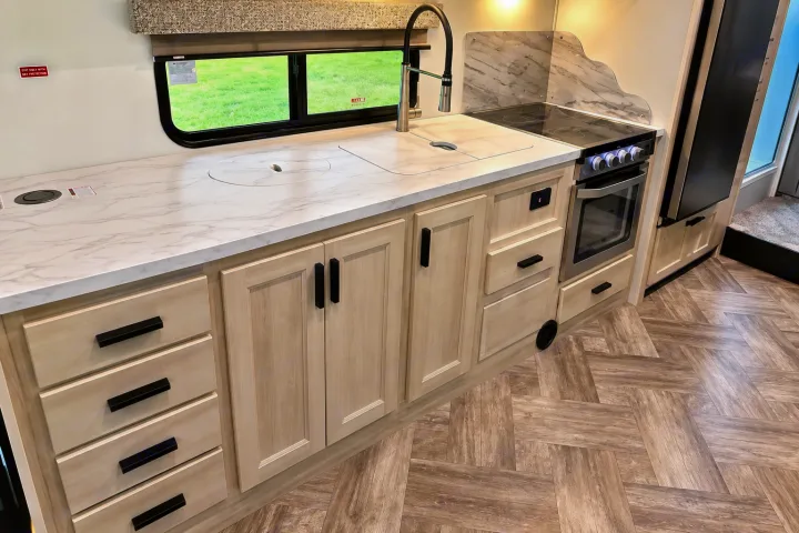 Modern RV rental kitchen with light wood cabinets, white marble-look counters, sink, stovetop, oven, and refrigerator.. Forester Classic 2021
