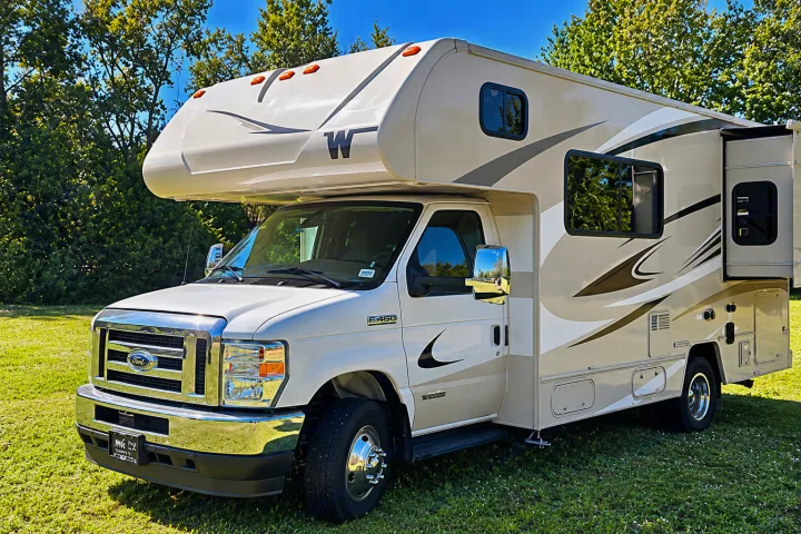 Enjoy this Class C rv rental! A beige Ford E-450 motorhome with an extended slide-out, parked on green grass.. Winnebago Minnie Winnie 2024