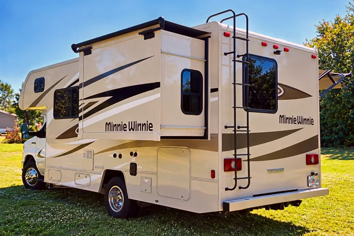 RV rental: A cream-colored Minnie Winnie motorhome with an extended slide-out and rear ladder parked on grass.. Winnebago Minnie Winnie 2024