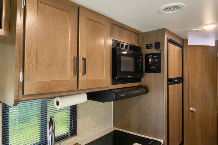 RV rental kitchen: light wood cabinets, Furrion microwave/hood, control panel, and fridge. Compact yet modern design.. Winnebago Minnie Winnie 2024