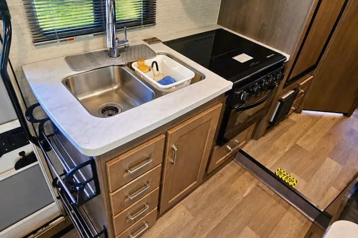 Compact RV rental kitchenette: stainless steel sink, stovetop/oven, light wood cabinets, and marble-look countertop for travel adventures.. Winnebago Minnie Winnie 2024