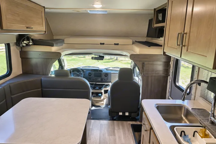 This rv rental interior features a dining area, kitchenette, driver's cabin, and overhead bunk bed.. Winnebago Minnie Winnie 2024