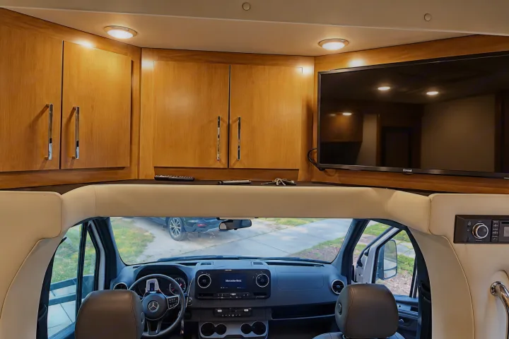 Inside a premium RV rental: Mercedes-Benz cockpit, sleek wood cabinets, and a mounted TV for entertainment.. Tiffin Wayfarer 2020