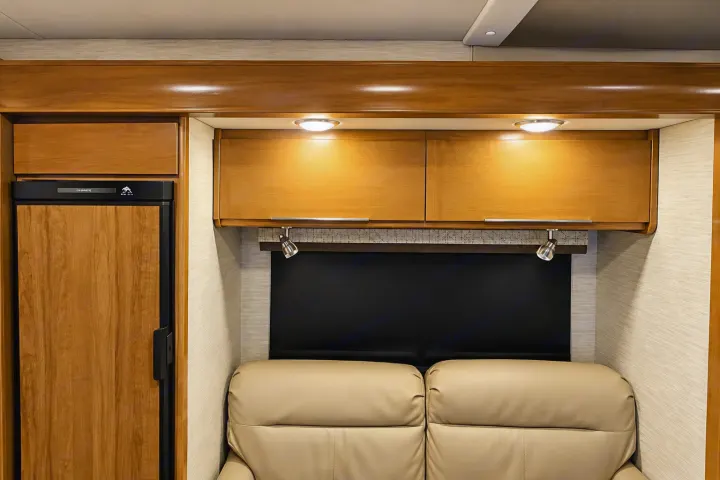 RV rental interior: integrated wood refrigerator, overhead cabinets, under-cabinet lighting, and plush seating.. Tiffin Wayfarer 2020