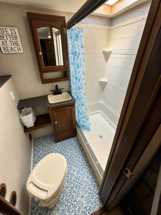 Step into this clean RV rental bathroom with a spacious shower, vanity, toilet, and stylish blue patterned floor.. Forest River Freedom 2017