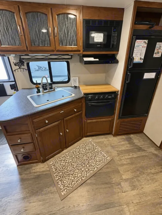 Comfortable RV rental kitchen with dark wood cabinets, a sink, microwave, stove, and refrigerator for your travels.. Forest River Freedom 2017