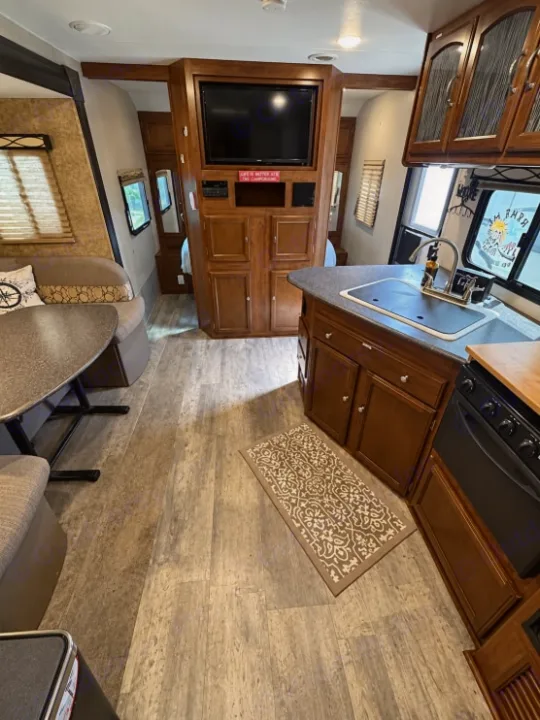 Interior of an RV rental showing kitchen with sink, dining area, and entertainment center with TV. Faux wood floor.. Forest River Freedom 2017