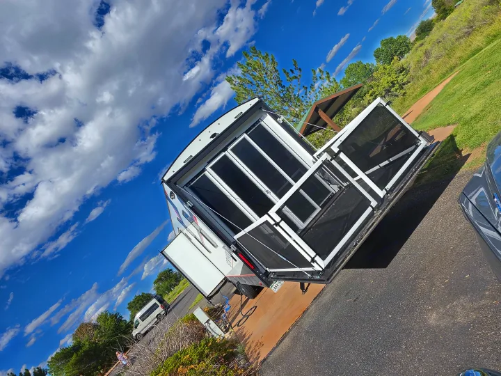 White rv rental travel trailer/toy hauler with open ramp door patio at a sunny campground under a blue sky with clouds.. Cruiser Rv Corp Stryker 2025