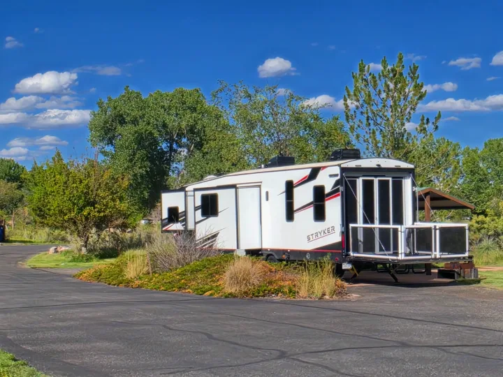 A white Stryker travel trailer, an rv rental, parked at a sunny campsite. It features a unique rear patio, with trees & a blue sky.. Cruiser Rv Corp Stryker 2025