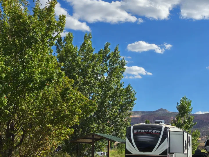 A 'Stryker' RV rental parked at a scenic campground with lush trees, a blue sky, and distant mountains under white clouds.. Cruiser Rv Corp Stryker 2025