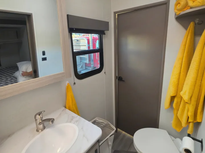 RV rental bathroom featuring a sink, toilet, mirror reflecting a bed, a window, and yellow towels.. Cruiser Rv Corp Stryker 2025