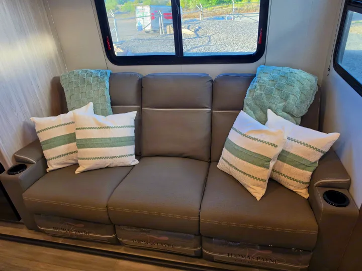 Comfortable RV rental interior featuring a gray Thomas Payne reclining sofa with cup holders, green & white pillows, and a window view.. Cruiser Rv Corp Stryker 2025