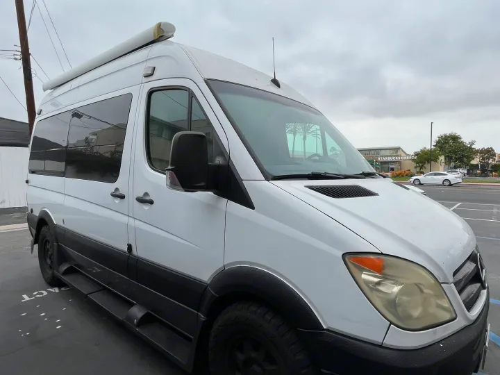 This white Mercedes Sprinter RV rental, with an awning and off-road tires, is ready for adventure in a parking lot near Starbucks.. Roadtrek Roadtrek Class B 2007