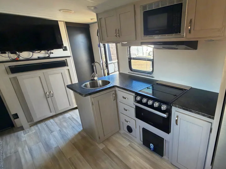 Bright rv rental interior showcasing a modern kitchen with a stove, oven, microwave, sink, and a TV entertainment setup.. Forest River Prime Time LE 2023