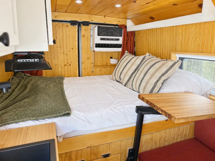 Inviting rv rental interior: warm wooden walls, a comfy bed with pillows, mounted TV, AC, and a handy swivel table.. Dodge Ram 2500 2024