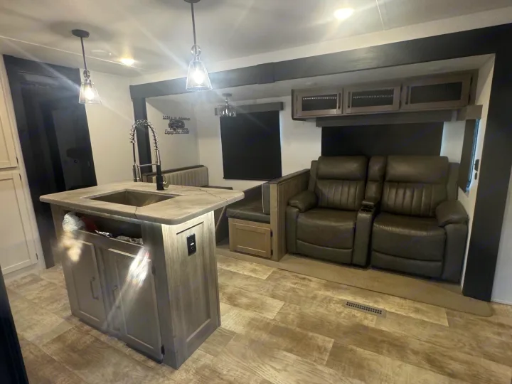Modern RV rental interior with kitchen island, dining booth, and comfy recliners, featuring pendant lights and wood-look flooring.. Forest River Palomino Puma 2025