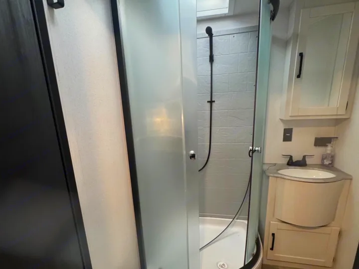 RV rental interior: Compact bathroom with corner shower, frosted glass door, and vanity sink.. Forest River Palomino Puma 2025