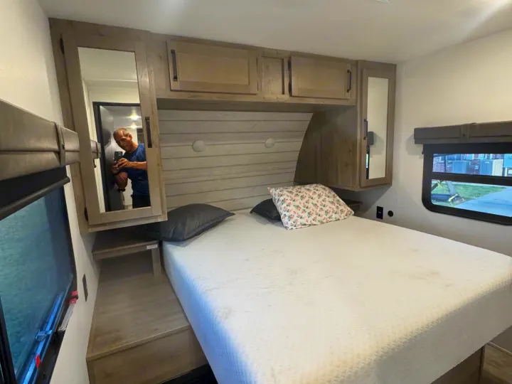 Cozy RV rental bedroom featuring a full bed, mirrored cabinet, and window. Ideal for comfortable travel & camping.. Forest River Palomino Puma 2025