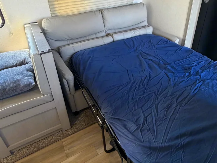 Cozy RV rental interior showing a gray sofa pulled out as a bed with a blue sheet, perfect for extra sleeping space.. Forest River Prime Time LE 2023