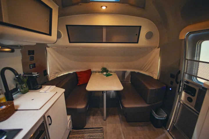 Cozy RV rental interior showing a compact dining area with brown benches, kitchen, and entrance.. Airstream Caravel 2022