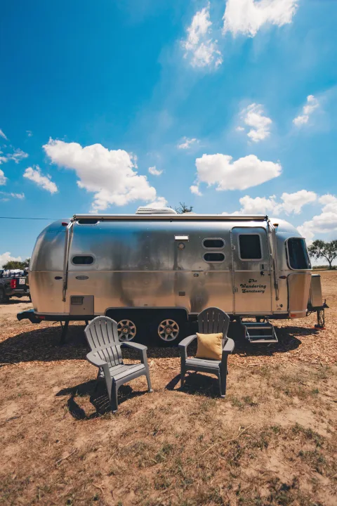 An Airstream travel trailer RV rental, "The Wandering Sanctuary," parked with outdoor chairs under a bright blue sky.. Airstream Caravel 2023