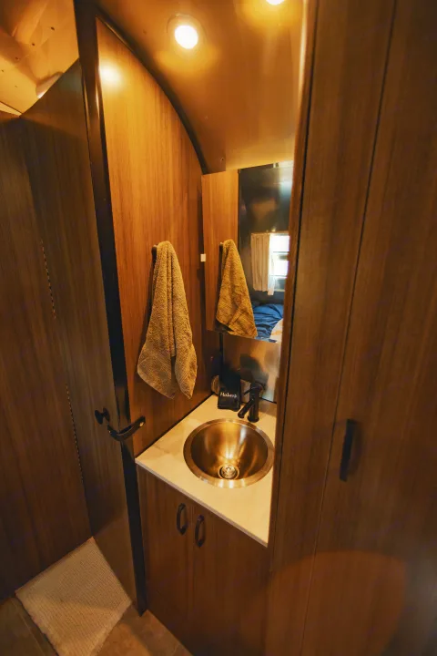 RV rental interior: A cozy, modern bathroom vanity with a stainless steel sink, dark faucet, and warm wood tones.. Airstream Caravel 2023