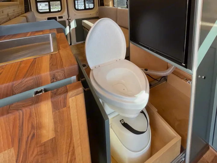 This RV rental interior features a composting toilet on a slide-out, an integrated kitchen sink, and a TV for convenient travel.. Off Grid Adventure Vans Sarge 2019