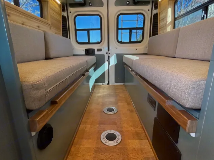 Clean RV rental interior with cozy bench seating/beds on both sides, a bright aisle, and wooden accents.. Off Grid Adventure Vans Sarge 2019
