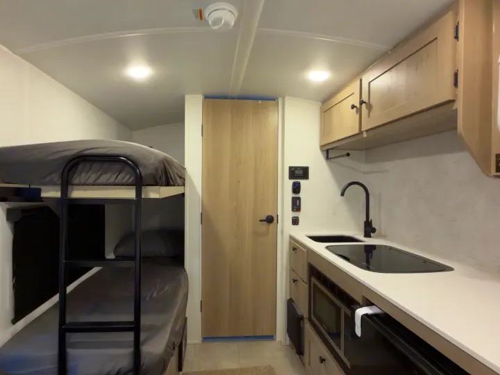 RV rental interior with bunk beds, a compact kitchen (sink, stove, microwave, cabinets), and a light wooden door.. Forest River Rockwood Geopro 2026