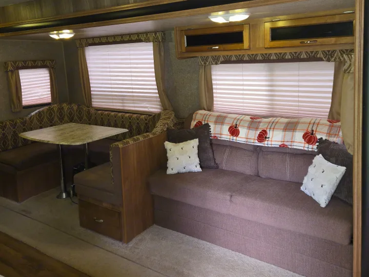 Cozy RV rental interior showing a dinette with table, sofa, cushions, and overhead storage. Ideal for travel.. Coachmen Catalina 2017