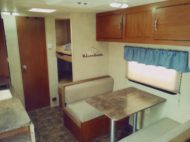 RV rental interior view: dinette, kitchen counter, bunk beds, overhead cabinets, and a door for compact living.. Forest River Salem Cruise Lite 2014