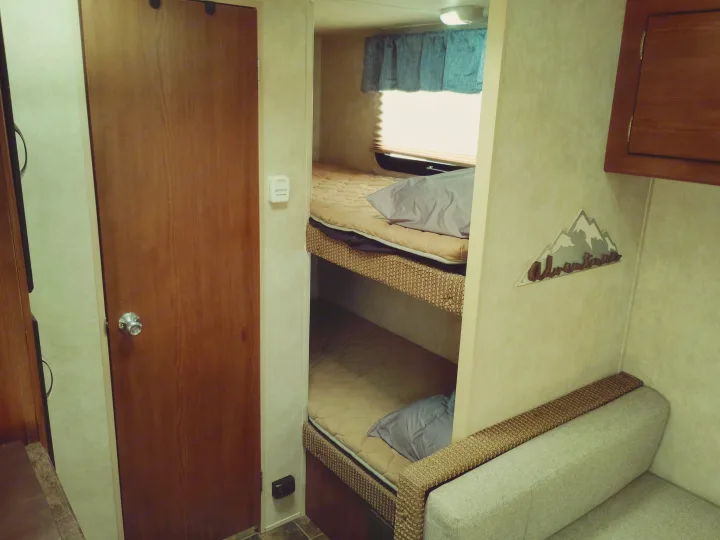 Cozy RV rental interior features bunk beds, a couch, a door, and an "Adventure" sign. Ideal for compact travel.. Forest River Salem Cruise Lite 2014