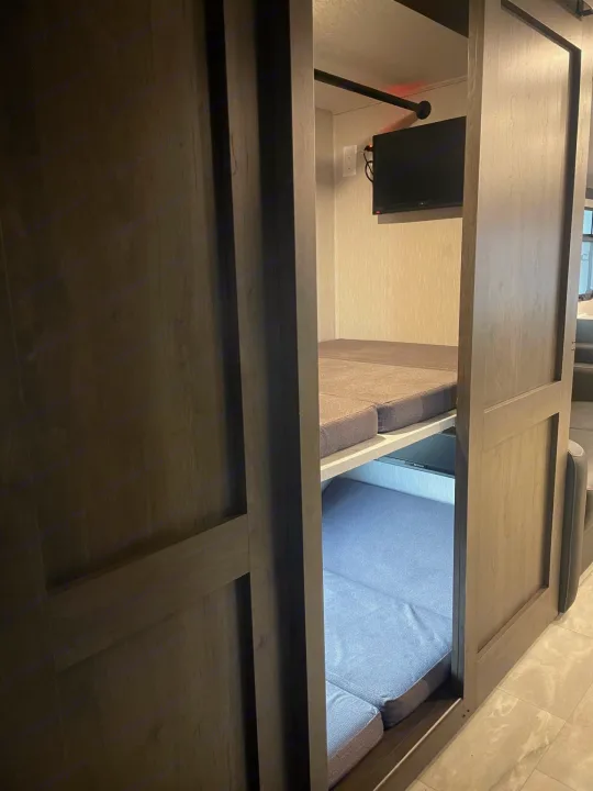 An RV rental interior with bunk beds. Two gray cushioned sleeping areas are visible, along with a wall-mounted TV.. Coachmen MIRADA 35ESF 2026