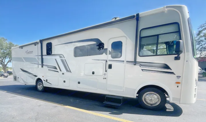Side view of a large, modern white and gray Coachmen Mirada RV rental, parked outdoors under a clear sky.. Coachmen MIRADA 35ESF 2026
