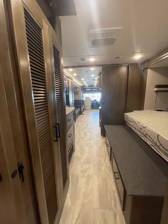 RV rental interior: A bright hallway leads past modern cabinetry & a bed with storage, towards the front cabin area.. Coachmen MIRADA 35ESF 2026