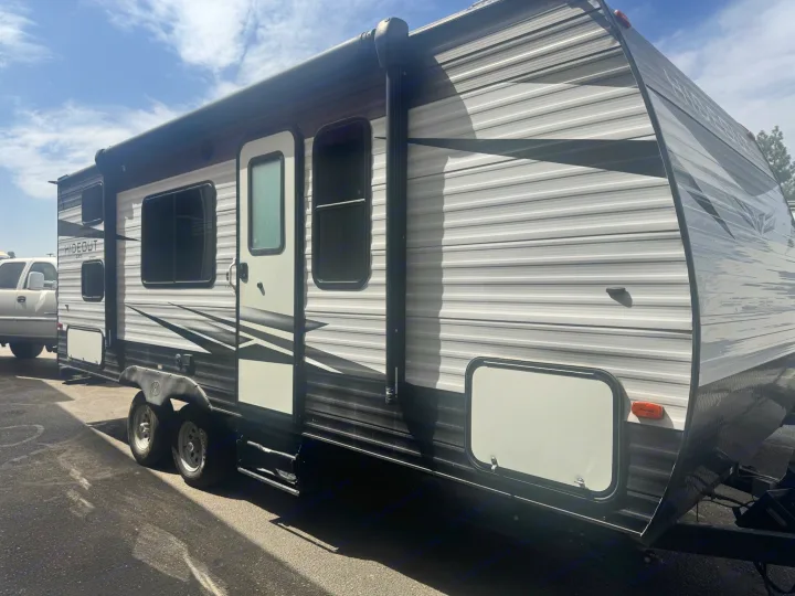 RV rental: Modern Hideout travel trailer, side view showing windows, door, and retractable awning under blue sky.. Keystone RV Hideout LHS 2019