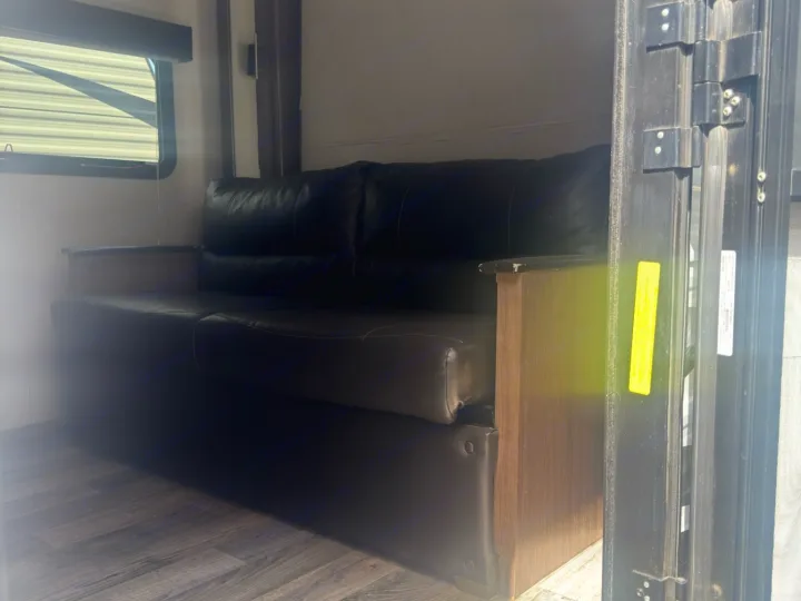 RV rental: Inside, a dark leather-look sofa with wooden armrests, wood-grain floor, and a window with blinds defines a cozy living area.. Keystone RV Hideout LHS 2019