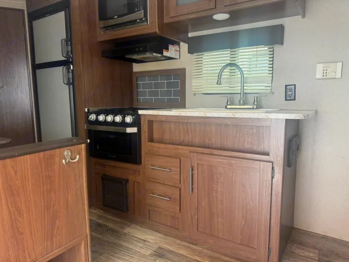 This RV rental kitchen offers a full setup: fridge, stove, microwave, sink, and cabinets, plus a fun octopus hook.. Keystone RV Hideout LHS 2019