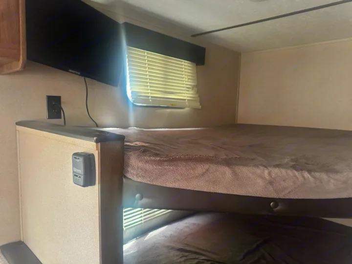 Cozy bunk beds in an RV rental, featuring a TV, window with blinds, and thermostat for comfort. Perfect for family trips.. Keystone RV Hideout LHS 2019
